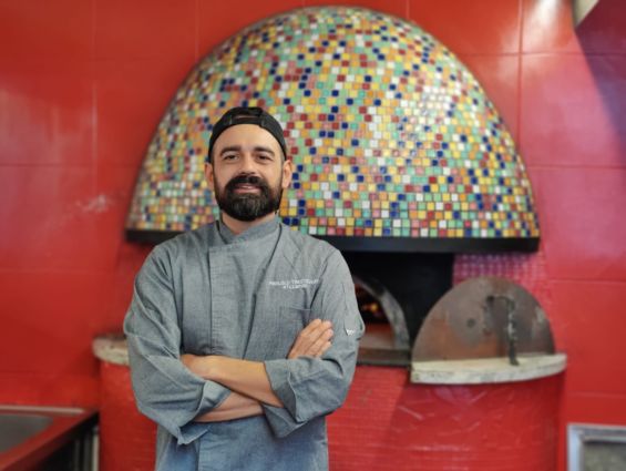 Pizzeria contemporanea: pizzaiolo davanti al forno a legna decorato con mosaico colorato.