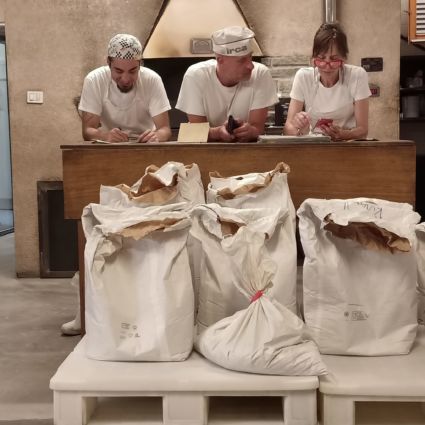 Preparazione pane GraniBurger Milano: sacchi di grani antichi e panettieri al lavoro.