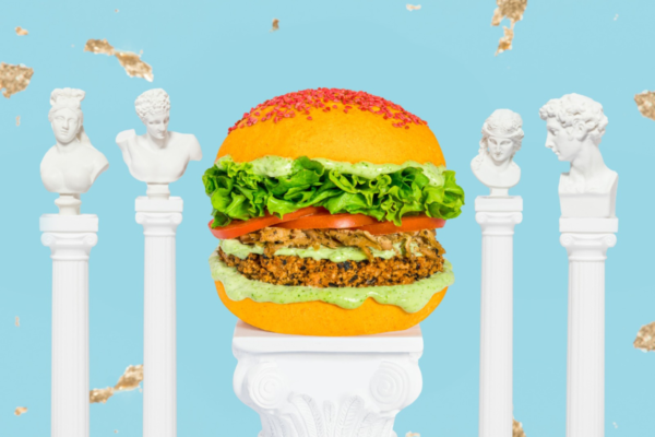 Burger vegano Flower Burger x Planted su piedistallo con statue. Collaborazione food, panino colorato.