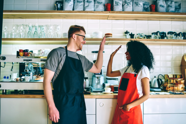 Team di ristorazione. Cobranding: barista e cuoca fanno high five in cucina.