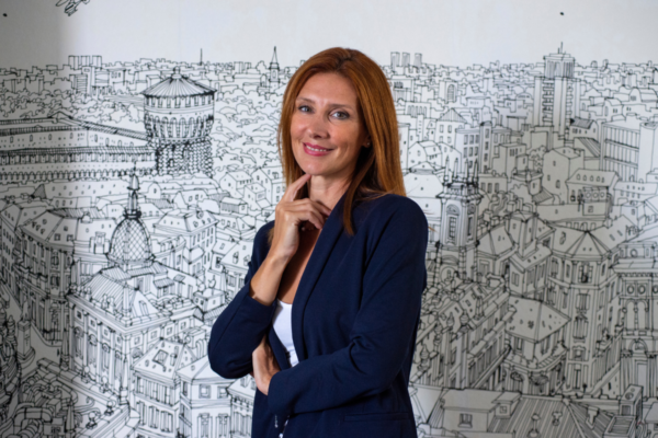 Donna, ruolo strategico acquisti hospitality. Manager sorridente, sfondo con disegno città.