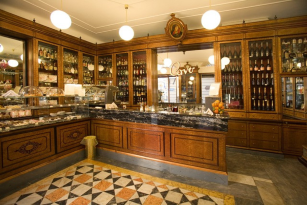 Interno locale storico: arredi originali in legno, vetrine con liquori e dolci, pavimento a scacchi. Attività dal 1954.