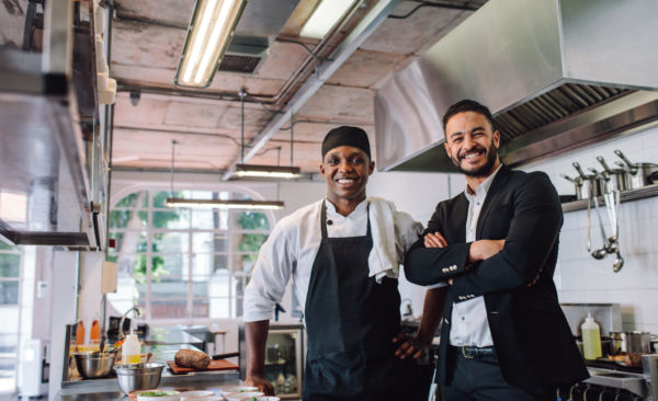 Chef e manager sorridenti in cucina. Assunzioni ristorazione in arrivo.