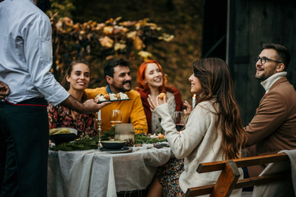 Trend di consumo: gruppo di amici a cena. Chef serve antipasti. Next normal, convivialità e socializzazione.