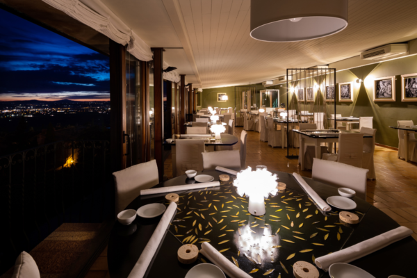 Interno ristorante elegante con vista notturna. Tavoli apparecchiati, illuminazione soffusa. Esperienza culinaria di lusso.