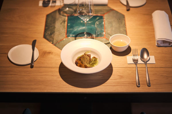 Ristorante Radici: cucina a km zero contro lo spreco alimentare. Tavolo con piatto gourmet e posate.