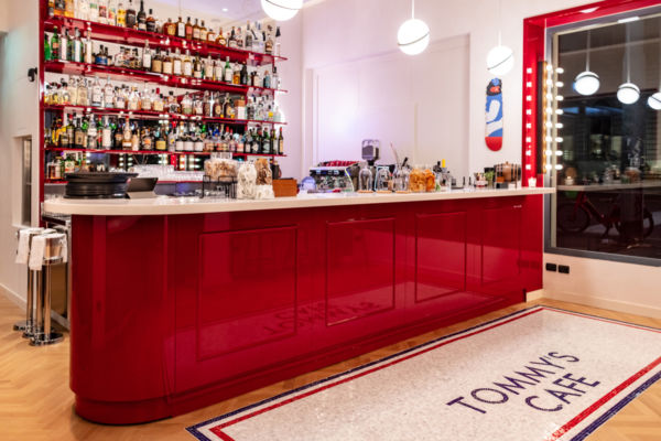 Bancone bar rosso Tommy's Cafe Milano. Design Tommy Hilfiger, scaffali con bottiglie.