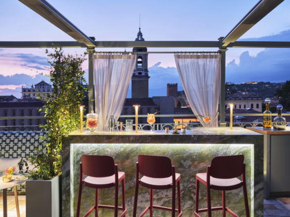 Terrazza ristorante a Verona con bar illuminato e vista panoramica sulla città al tramonto.