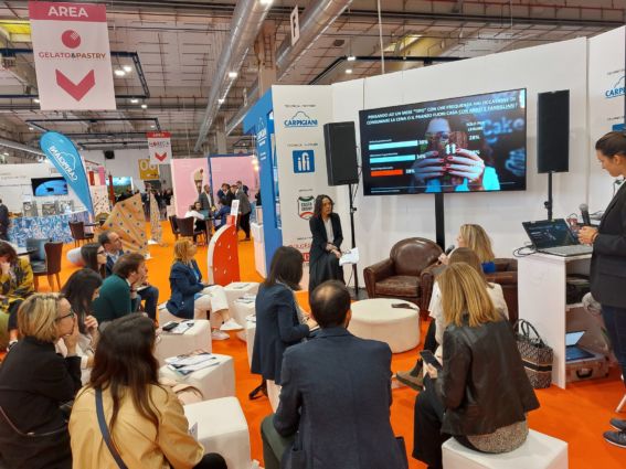 Presentazione dessert a Cibus Connecting Italy. Pubblico, schermo con dati sui consumi. Focus su gelato e pasticceria.