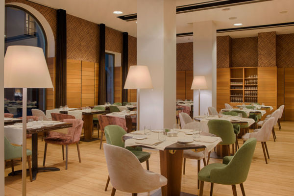 Interni La Pista Bistrot, Hotel NH Collection Torino Santo Stefano. Tavoli apparecchiati, sedie colorate, lampade.