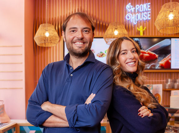 Fondatori di Poke House sorridono. Ristorante poke con lampade di design e logo al neon. Fatturato a 100 milioni di euro.