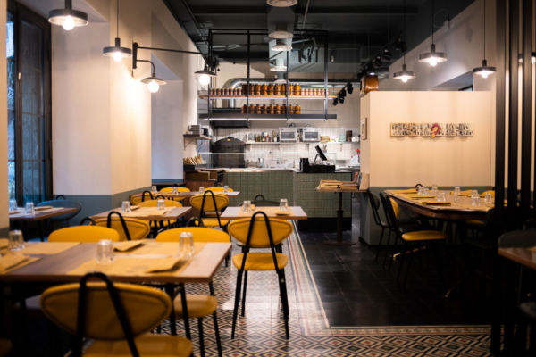 Interno del ristorante Poormanger, tavoli apparecchiati e cucina a vista. Ambiente accogliente.