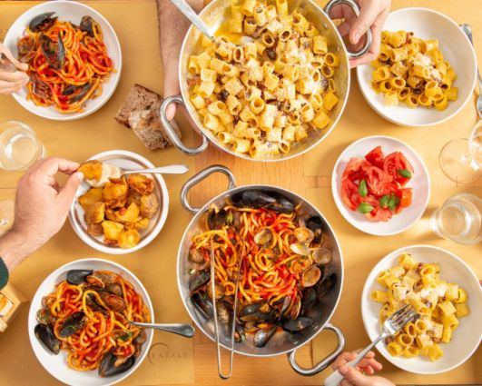 Tavola imbandita Eataly: pasta artigianale, olio EVO, frutti di mare, pomodori e patate. Celebrazione cucina italiana.