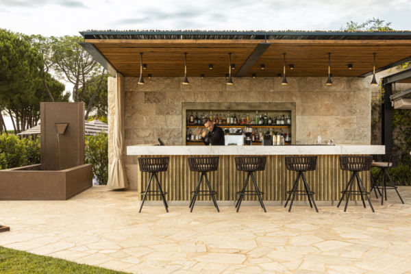 Bar Ecrù Castelfalfi: elegante bar esterno con sgabelli, cocktail e fontana. Relax e lusso per l'Hamburger Day.