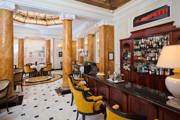Interno elegante del Café Marinetti. Bar fornito, tavoli apparecchiati e dettagli di lusso. Hotel di charme.