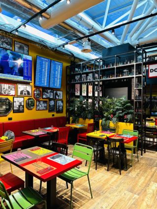 Interno Doppio Malto a Fiumicino. Arredamento colorato, tavoli vivaci, atmosfera accogliente. Lagardère Travel Retail.