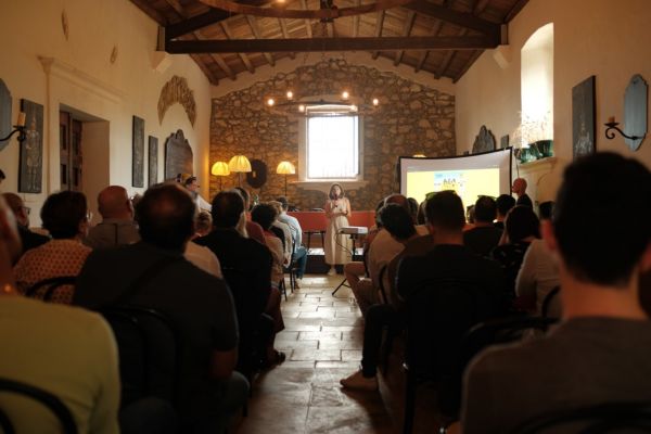 Evento Farina Petra: presentazione Adotta un Raccolto con pubblico. Donna parla al microfono, schermo proietta immagini.