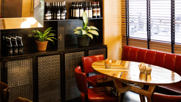 Interni dell'Osteria Pandenus con Enrico Bartolini: tavolo in legno, divanetto rosso e scaffale con vini.