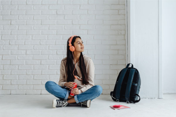 Ragazza con cuffie e Coca-Cola. Fondo venture capital per la sostenibilità. Zaino e muro di mattoni.
