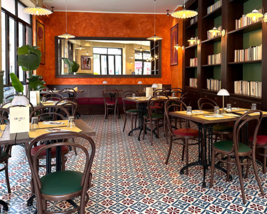 Interno accogliente del ristorante Pizzium Verona. Arredamento vintage, tavoli apparecchiati e scaffali con libri.