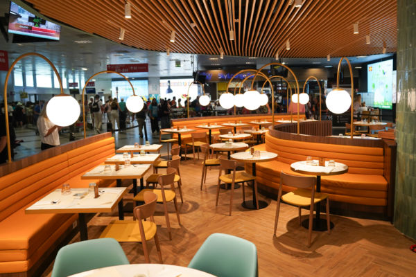 Interno Food Hall Autogrill, aeroporto Palermo. Tavoli apparecchiati, sedute imbottite, illuminazione moderna.