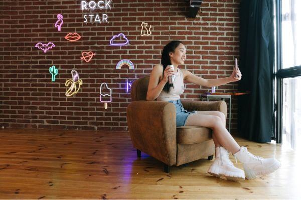 Marketing ristorazione USA: donna fa selfie su poltrona. Neon Rock Star e simboli. Stile cool e moderno.