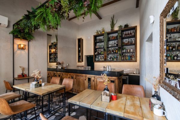Interno bar Corner: tavoli in legno, sedie in pelle, bancone bar fornito e decorazioni vegetali. Design accogliente.
