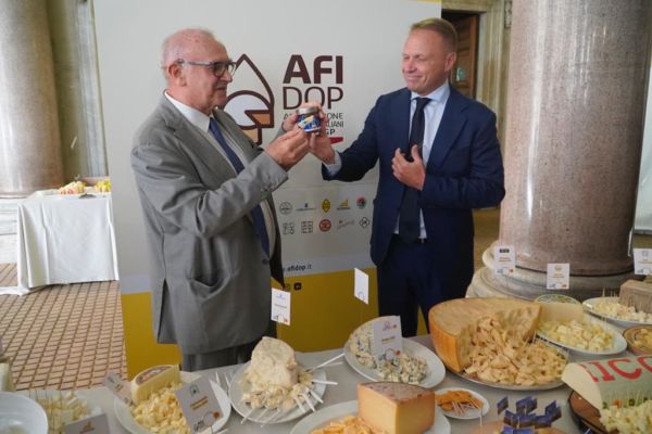 Evento Afidop: accordo per i formaggi DOP italiani. Uomini con confezione e tavola imbandita di formaggi tipici.