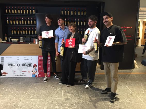 Amaro Lucano pronto per Singapore: team con bottiglie e cartelli finalista.