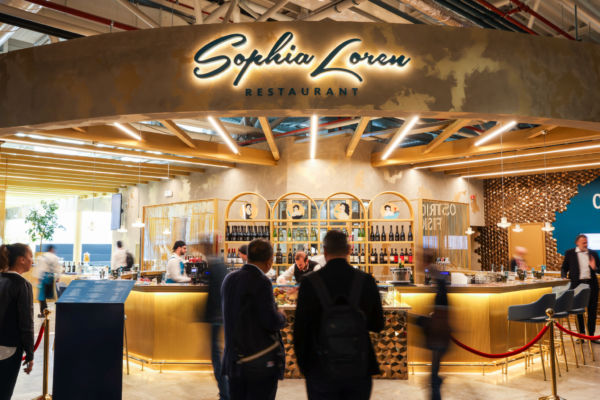 Autogrill Fiumicino: Ristorante Sophia Loren. Design elegante, bar dorato, atmosfera accogliente. Travel retail di lusso.