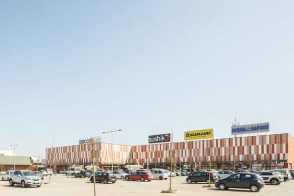 Retail Park Roero: parcheggio auto pieno di fronte al centro commerciale con negozi e insegne.