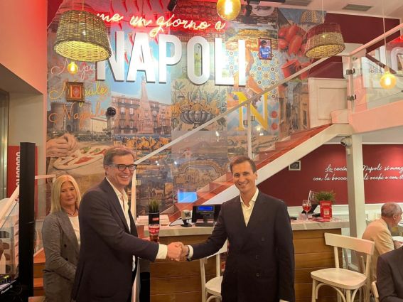Accordo Rossopomodoro e Coca-Cola. Uomini si stringono la mano nel ristorante. Napoli sullo sfondo.