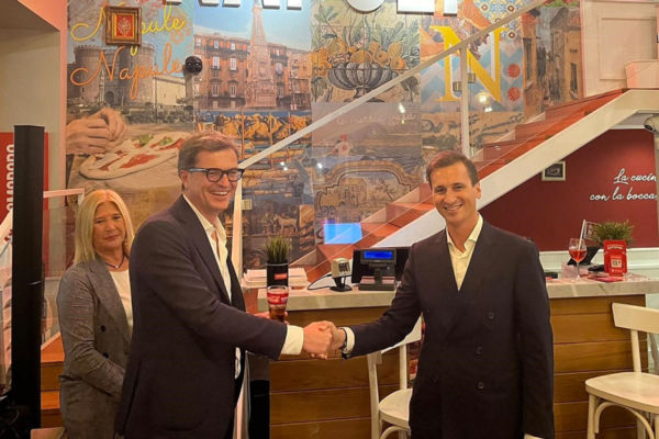 Accordo Rossopomodoro e Coca-Cola. Uomini si stringono la mano. Ristorante con murales di Napoli sullo sfondo.