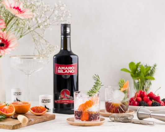 Amaro Silano: bottiglia, bicchieri con cocktail, agrumi e decorazioni. Tradizione e qualità calabrese.